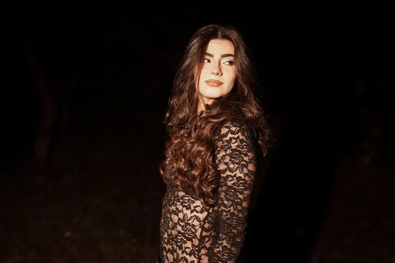 Portrait of a woman in a black lace dress at night, looking over her shoulder with long wavy hair.