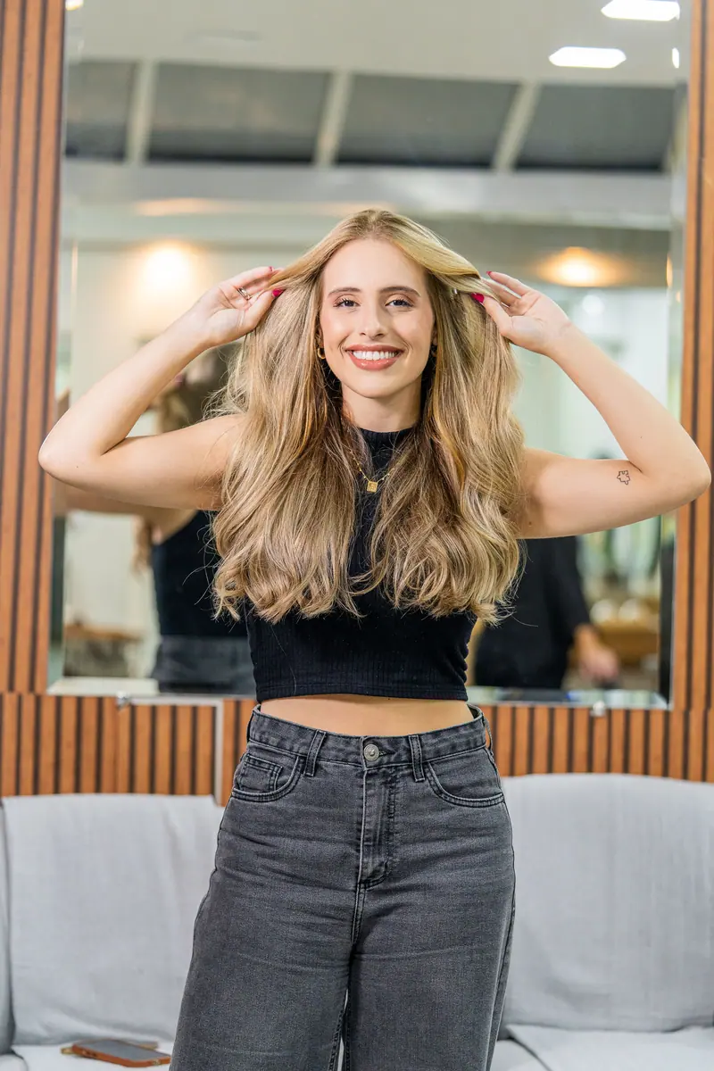 A cheerful woman with long blonde hair poses confidently in a salon setting.