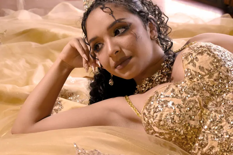 A woman lies gracefully in a sparkling golden gown, adorned with a tiara, exuding elegance and glamour.