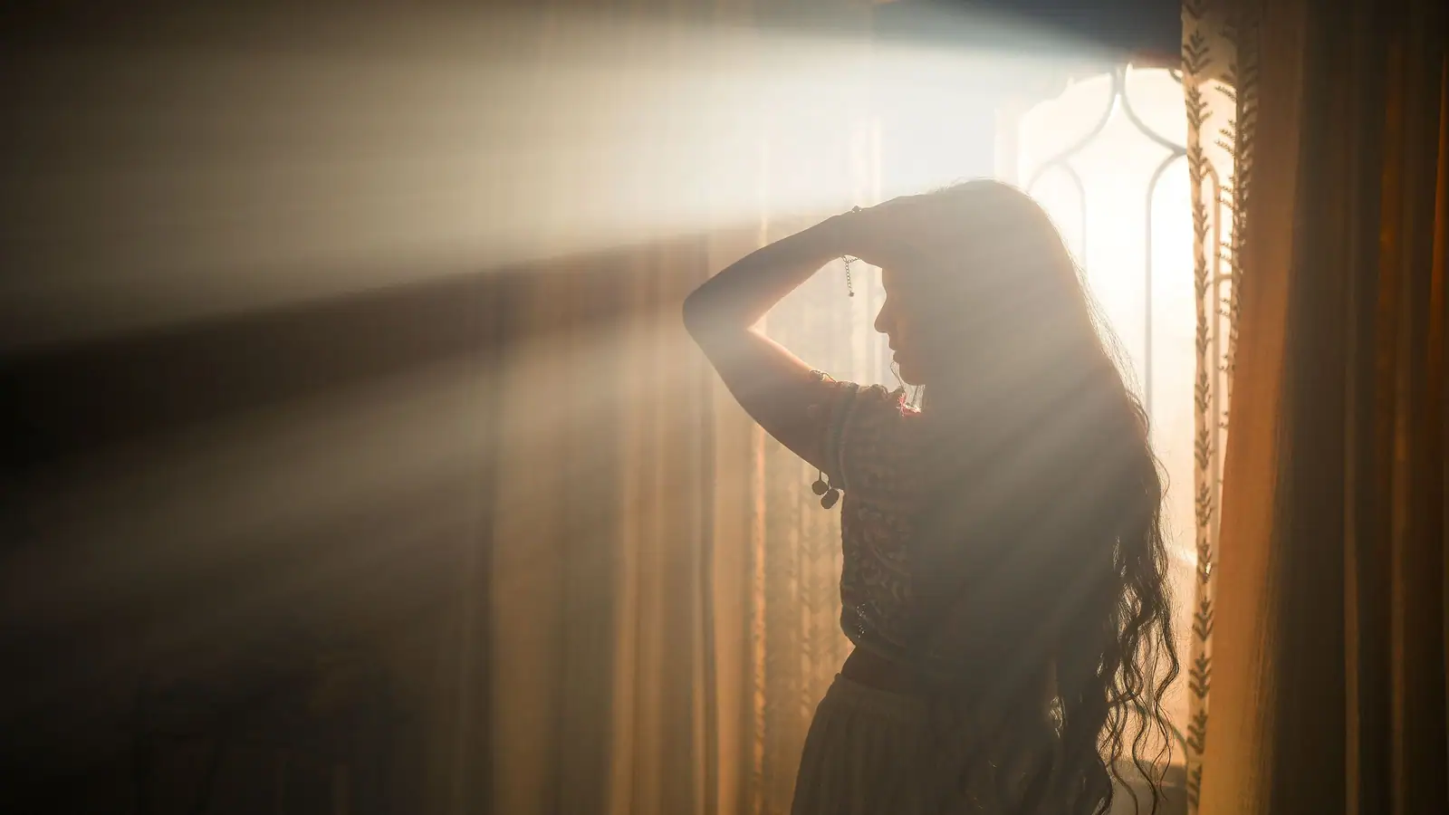 A woman in silhouette lifting her long hair in window light, face turned away
