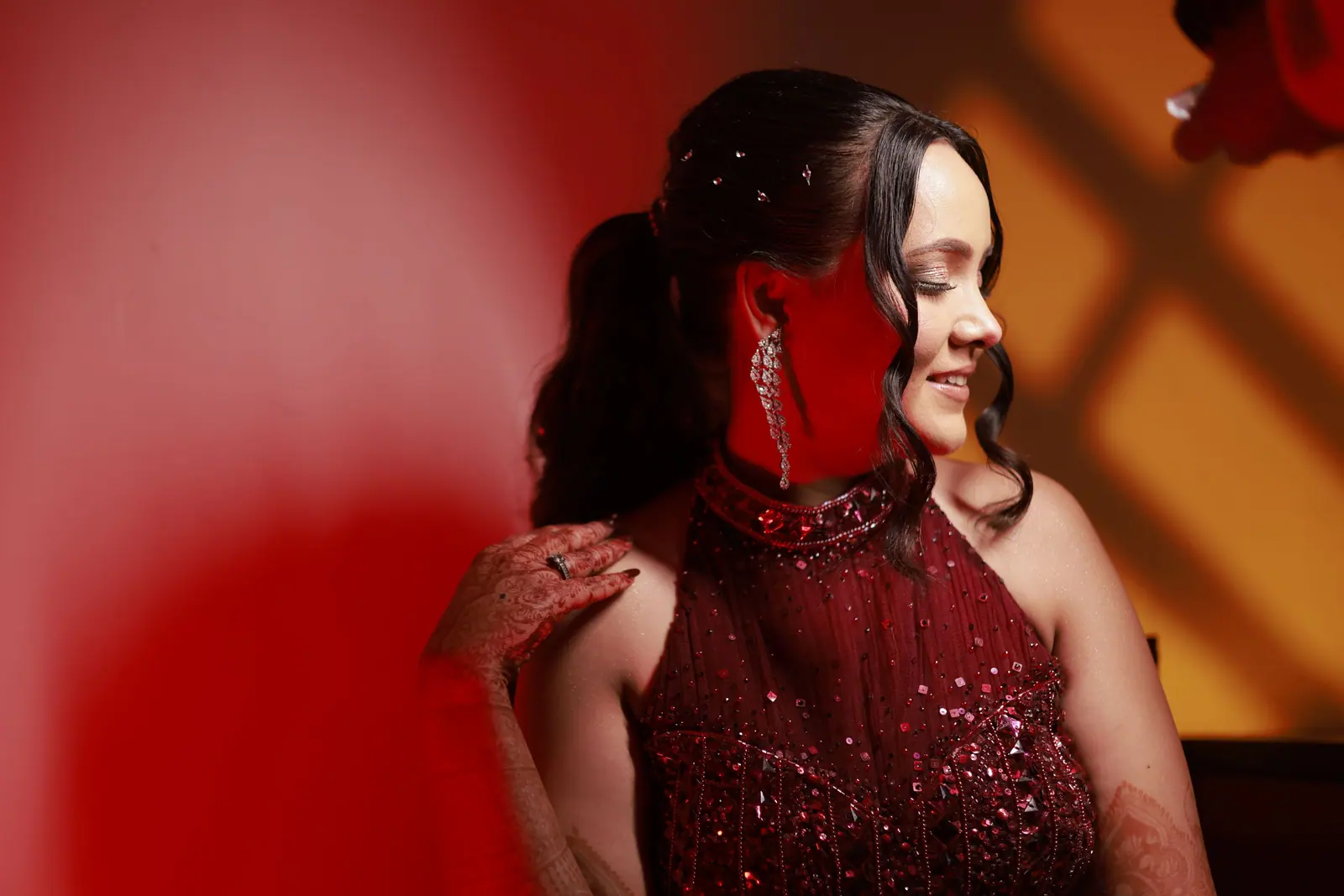 Woman with long, glossy dark hair and a red sequin dress against a deep red wall