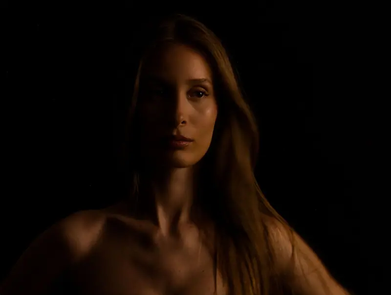 Moody low-key portrait of a young woman with a shadowed face and flowing hair.