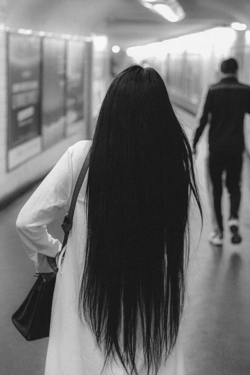 Black and white photo of a woman with long hair walking in an underground subway tunnel.