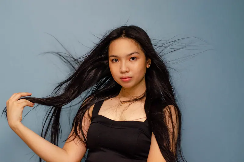 Studio portrait of a young woman with long black hair posing confidently against a blue backdrop.
