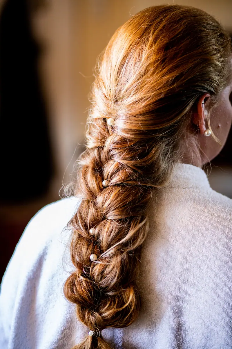 A woman with a stylish braided hairstyle featuring long, brown hair, captured indoors with soft lighting.