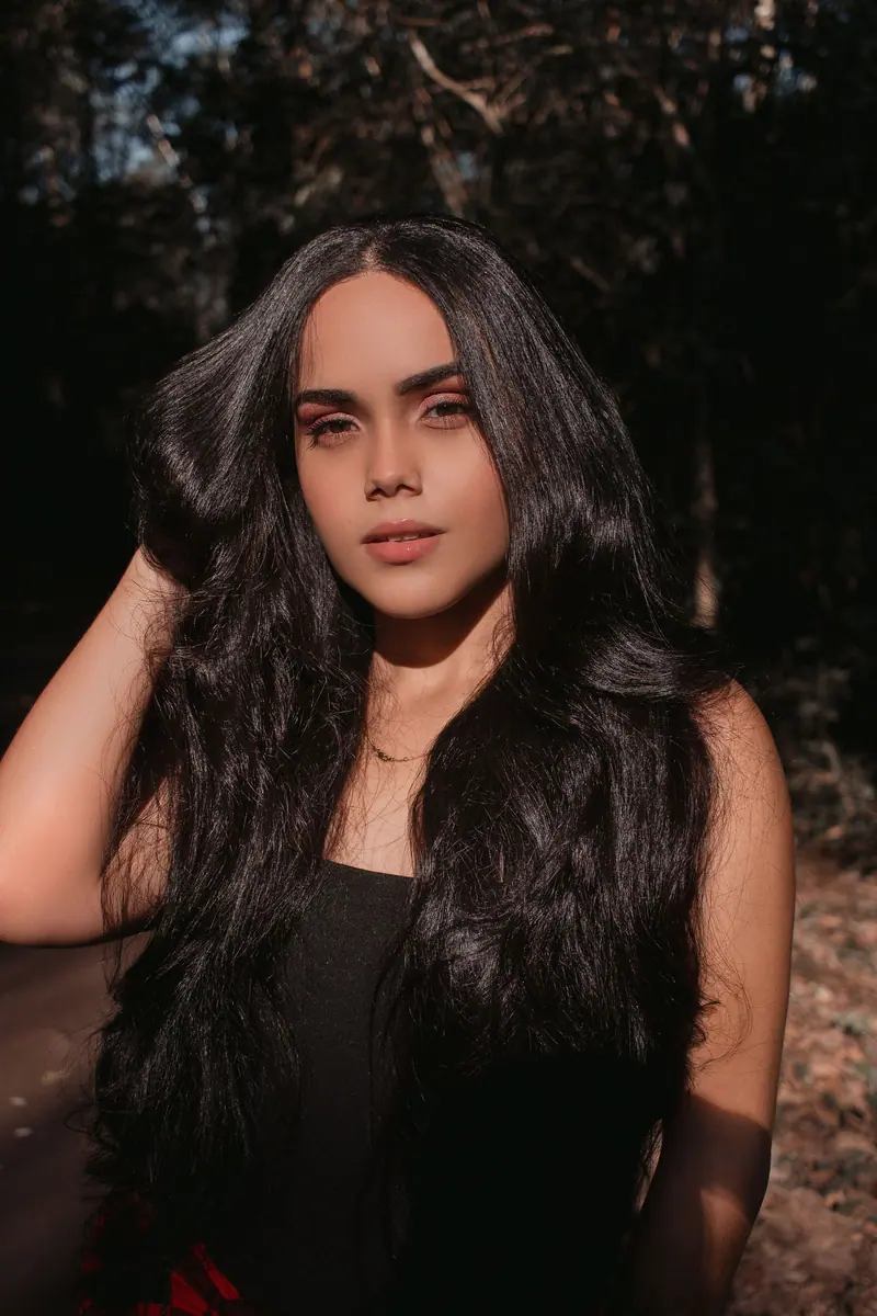 A beautiful woman posing in natural sunlight with lush hair, captured outdoors.