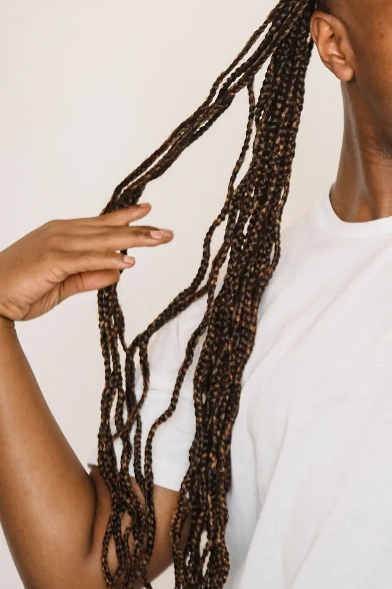 Person wearing a white shirt, holding long braided hair against a plain background.