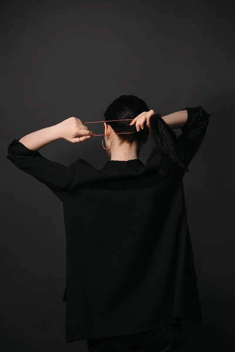 A woman with dark hair tied in a ponytail against a black background in a minimalist style.