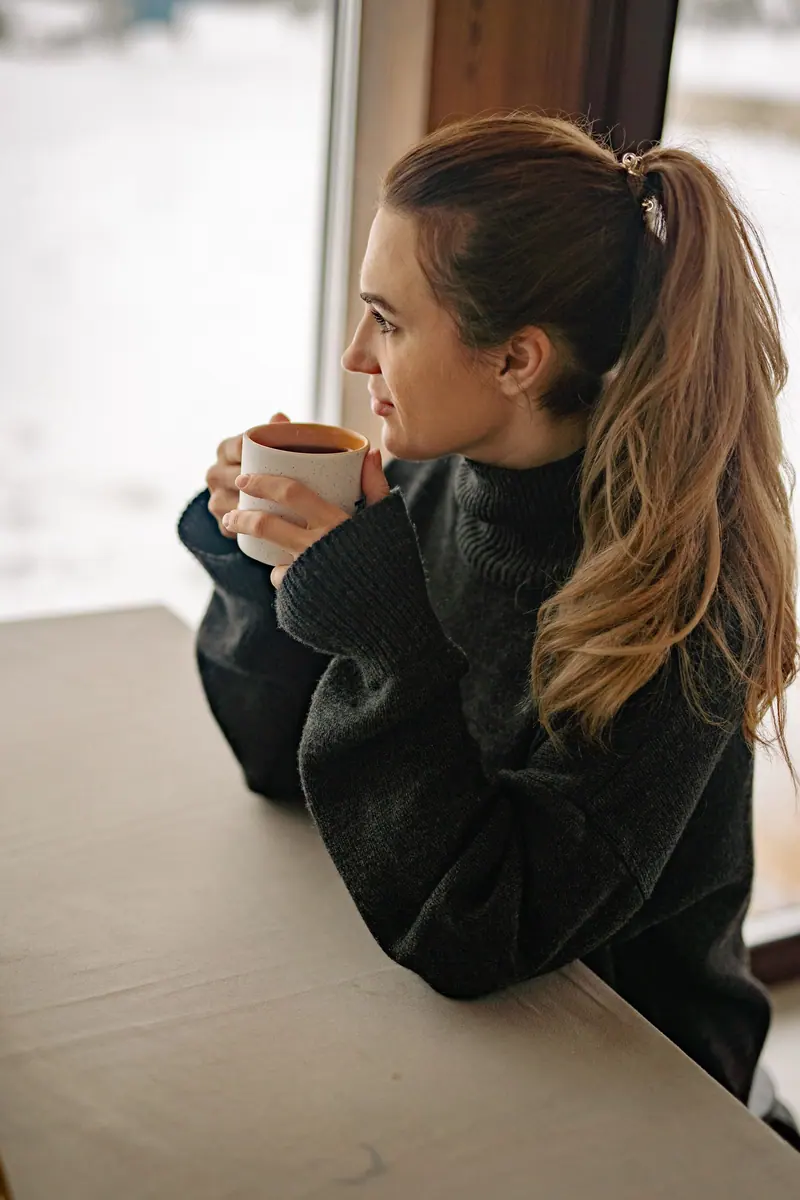 Woman enjoys a peaceful moment with a warm drink at home, embracing a cozy atmosphere by the window.