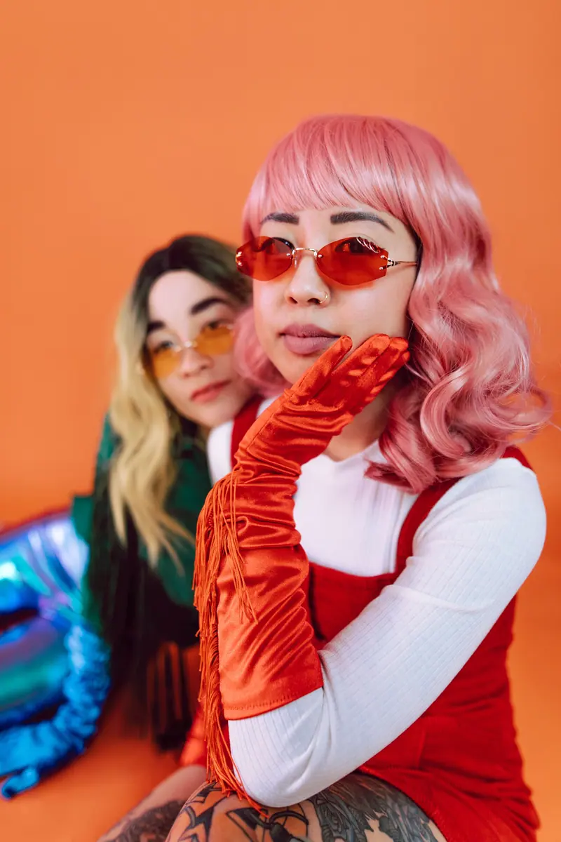 Two friends in pink and blonde wigs on an orange backdrop