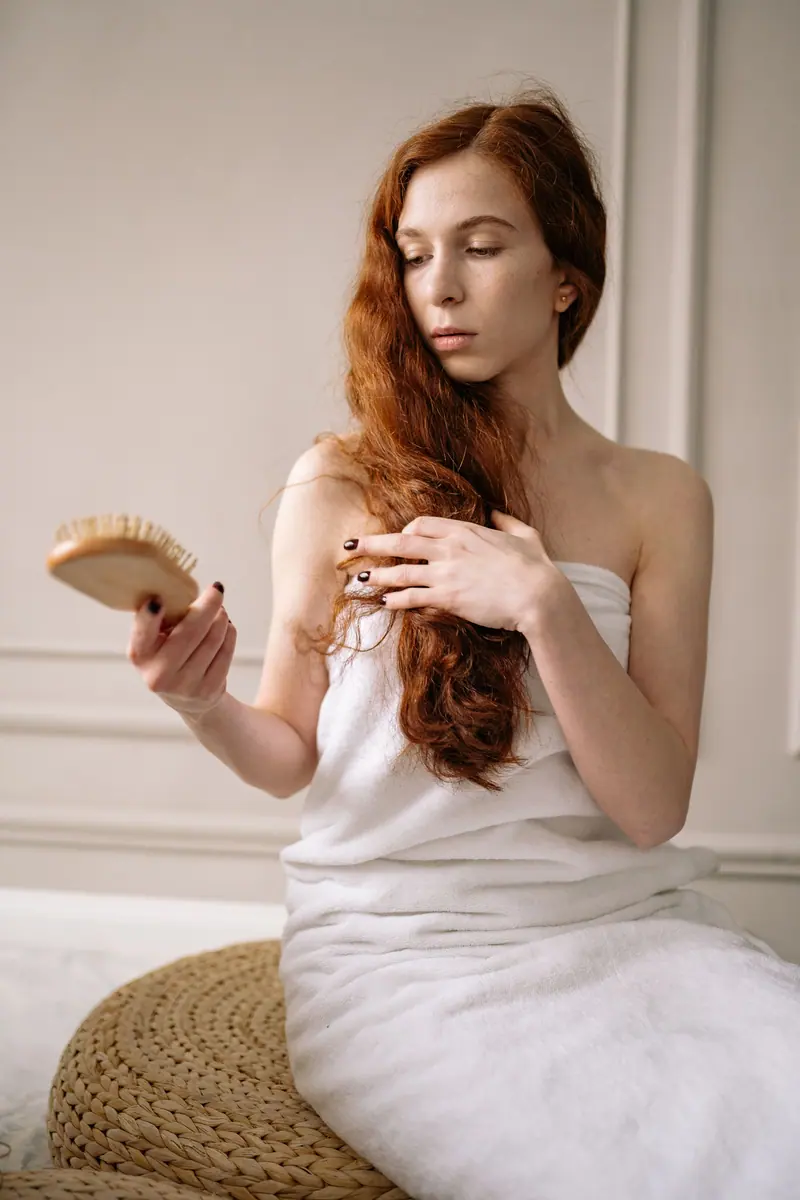 Woman brushing long copper hair after a wash, wrapped in a towel
