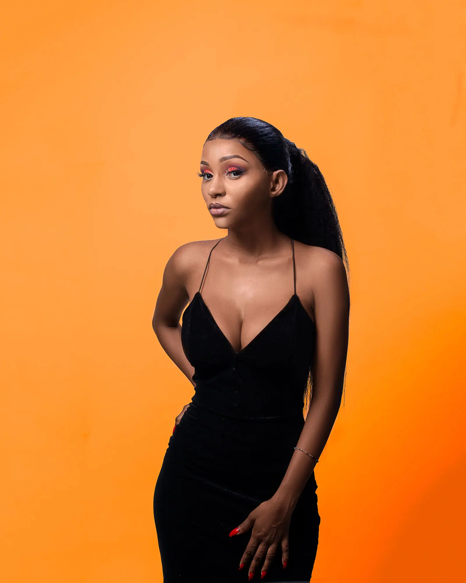 Woman with a long, sleek extended ponytail in a black dress against a warm orange backdrop