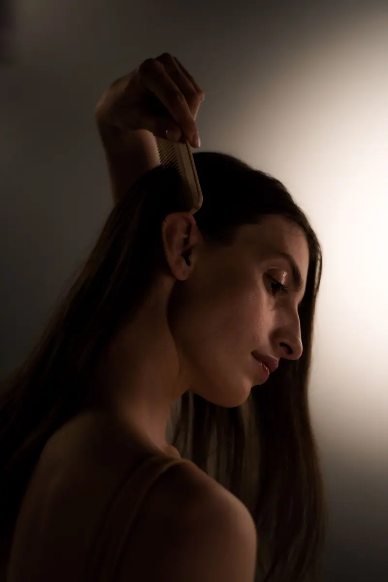 Close-up of a woman brushing her hair in a dimly lit setting, focusing on a self-care routine.
