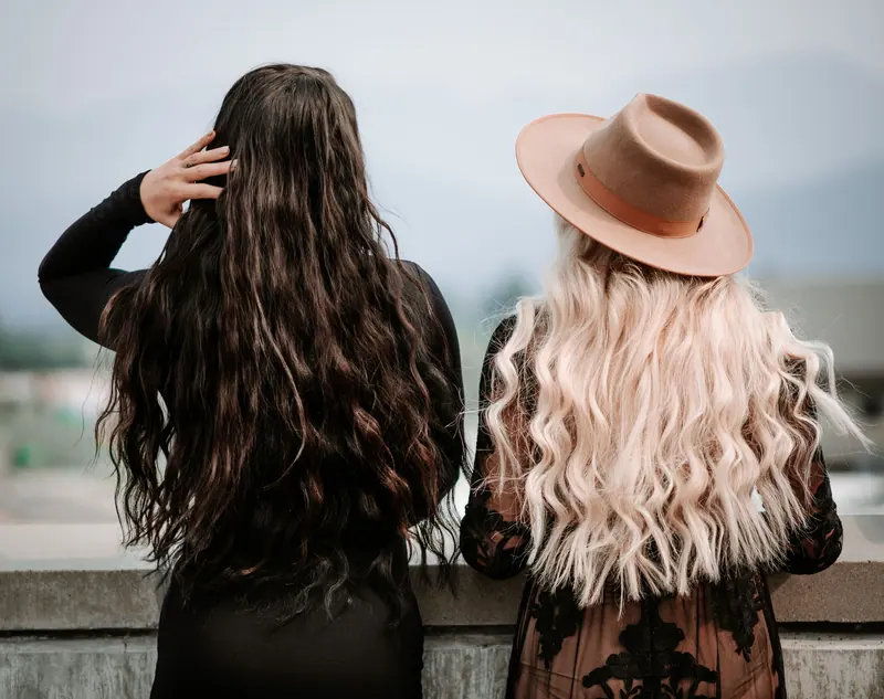 Two stylish women with long wavy hair standing on a rooftop, one in a fedora.