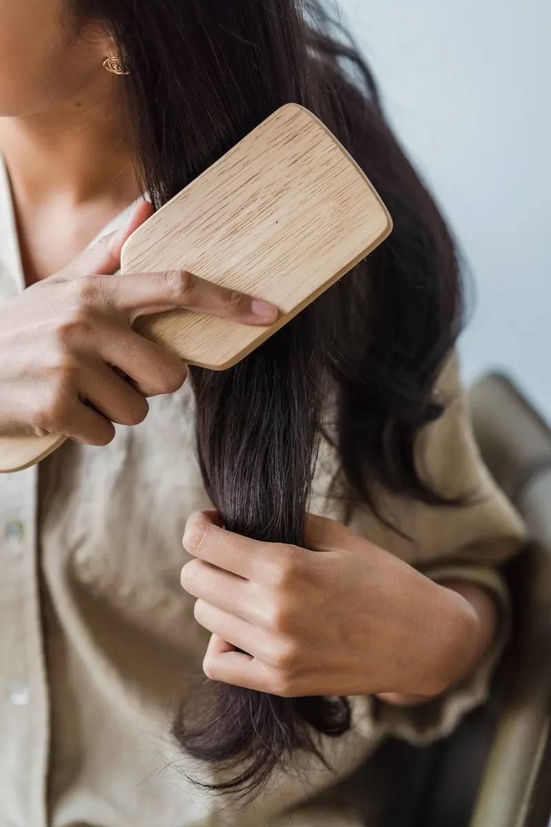 Close-up of a woman brushing her long dark hair with a wooden brush indoors.