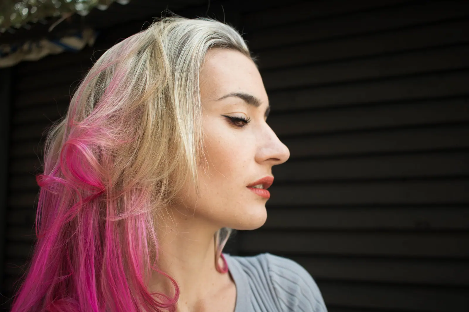 Profile of a woman with a platinum-to-hot-pink color melt against a dark backdrop