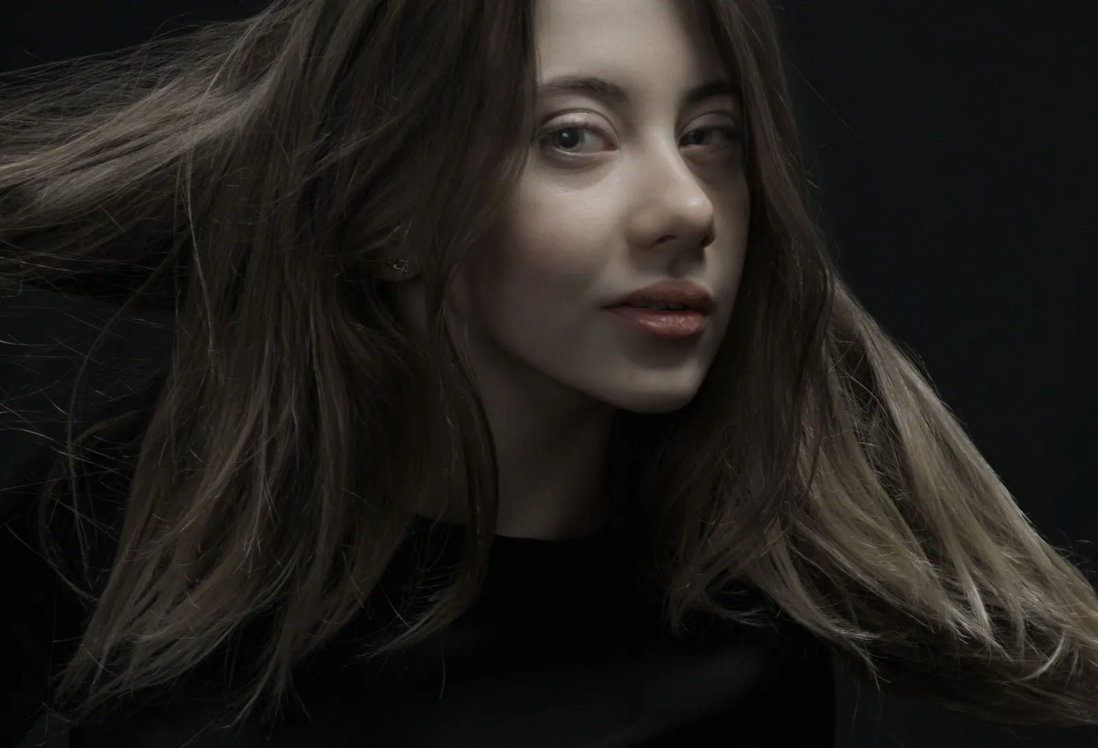 Editorial portrait of a woman with long, flowing, glossy hair in low moody light