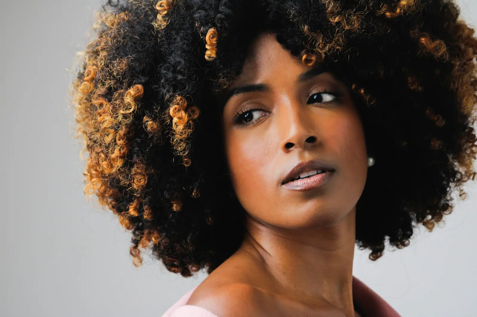 Woman with a voluminous honey-tipped natural curl crown, looking over her shoulder