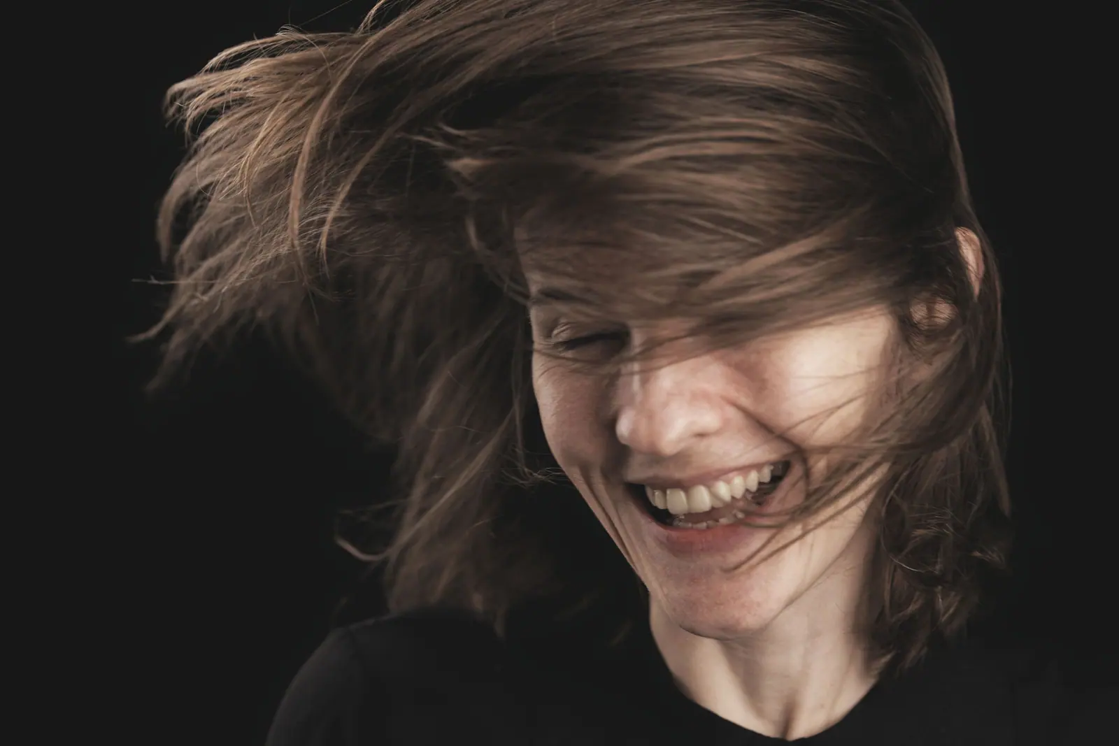 Laughing woman with a fresh cut swinging through her hair against a black backdrop