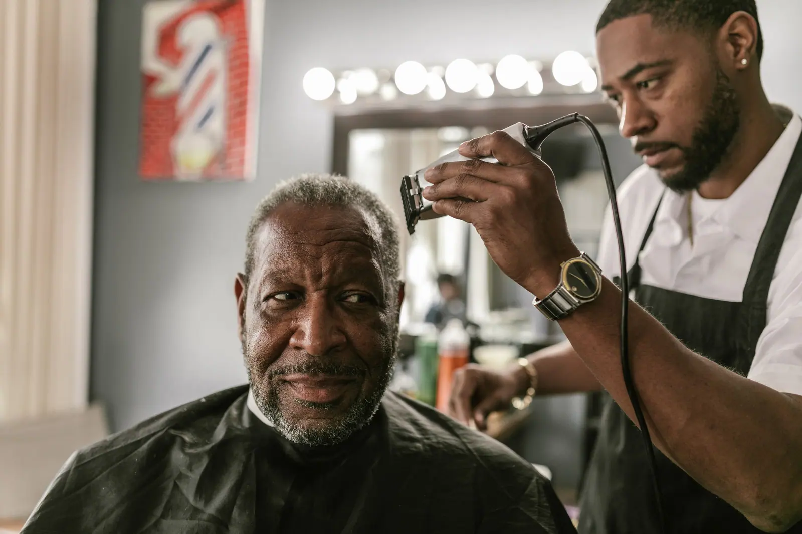 Barber taking a clipper to a senior client’s cut in a classic barbershop