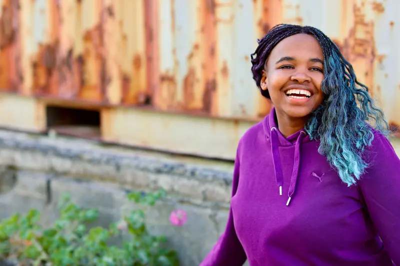 A happy woman in a purple hoodie with colorful hair, smiling outdoors. Vibrant and cheerful mood.