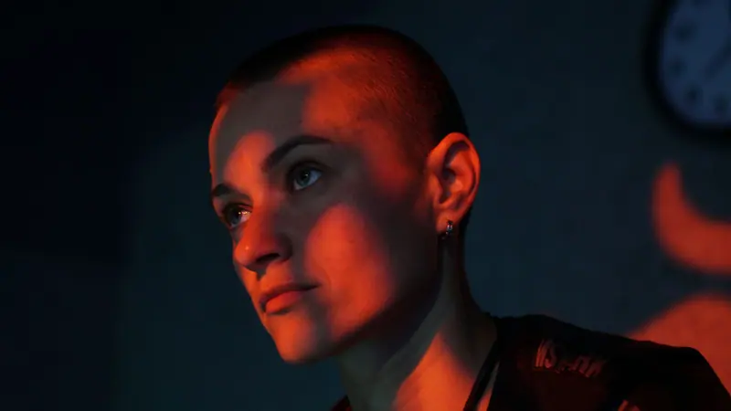 Bold portrait of a woman with shaved head in moody lighting.