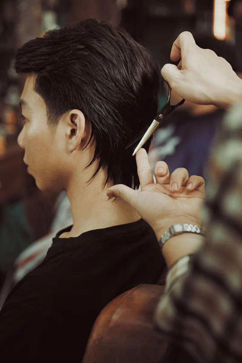 Close-up of a hairstylist giving a haircut to a young man at a salon.