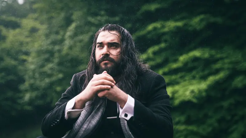 Long dark hair and beard against deep green trees