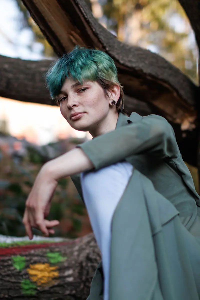 Stylish person with short green hair posing in an outdoor setting.