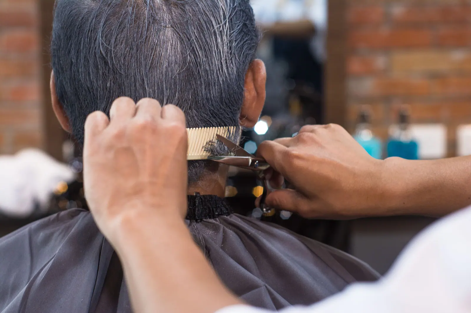 Detailed close-up of a barber clipping an adult's hair with scissors and comb in a modern salon setting.