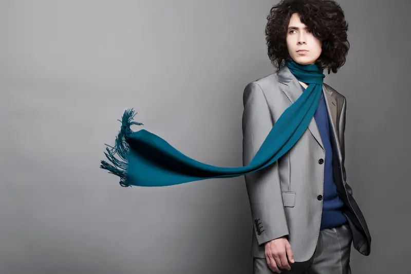Person with big dark curls and a grey suit, teal scarf flying