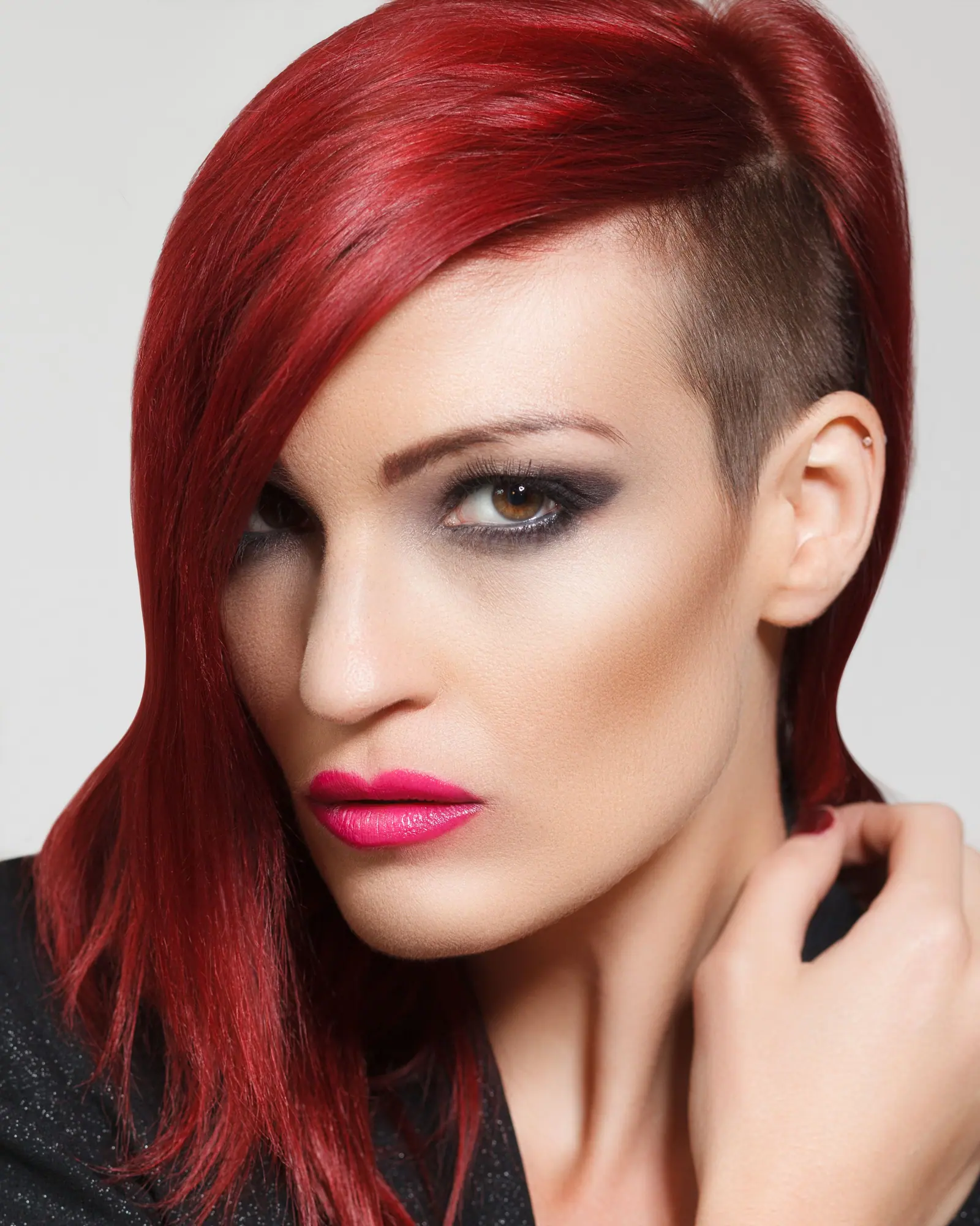 Woman with a sharp, asymmetric red cut and a shaved side, in close-up against a pale wall