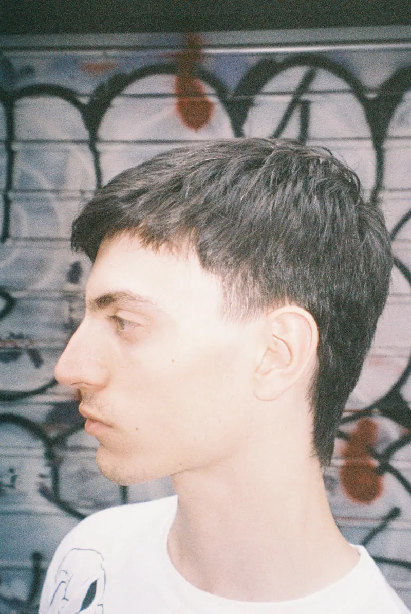 Side profile of a young man standing against a graffiti background.