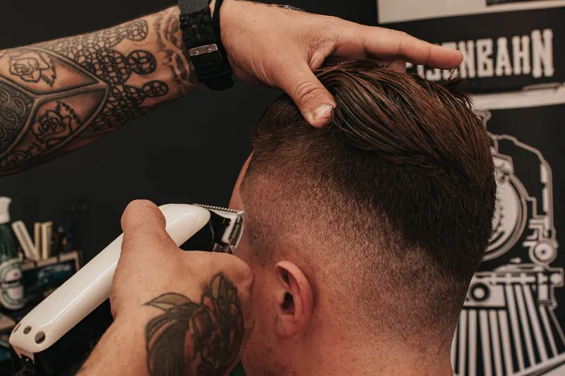 Barber's tattooed hands shaping a skin fade