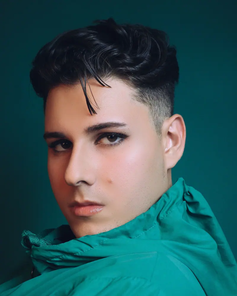 Smiling person with makeup against a teal backdrop