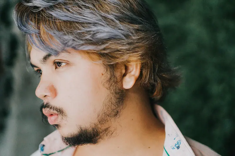 Close-up profile portrait of a young man with stylish hair, beard, and mustache.