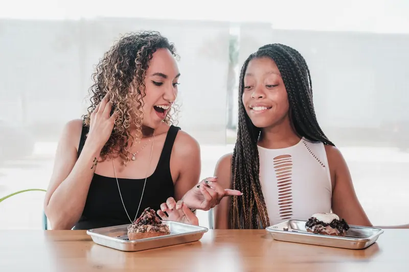 Two women sharing a moment over dessert, smiling and laughing at a cafe.