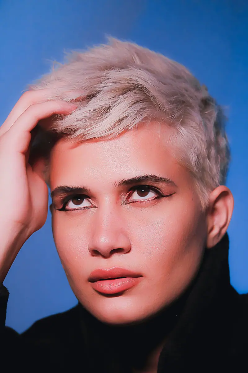 Close-up portrait of a person with short blonde hair against a blue background.