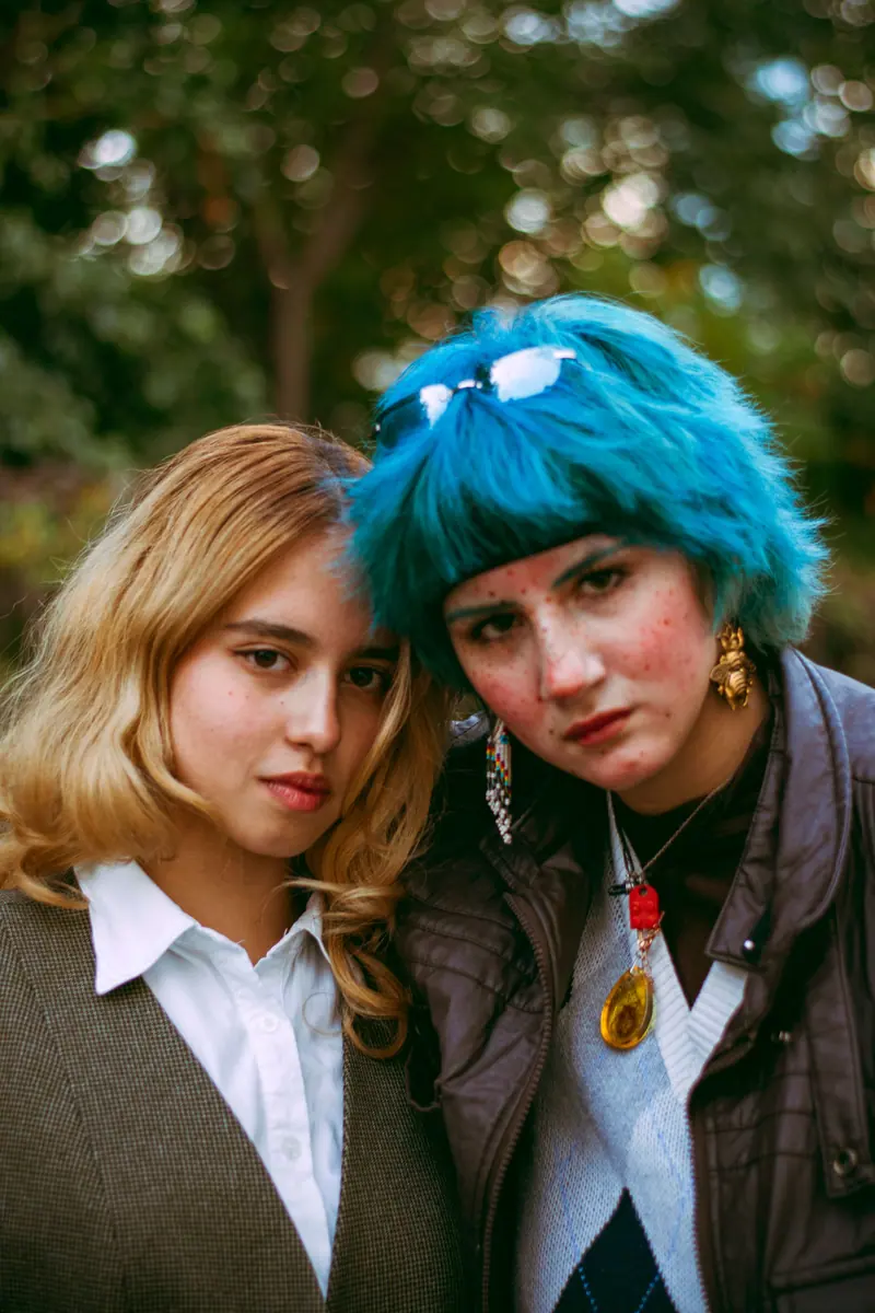 Two young women with unique hairstyles posing confidently in an outdoor setting.