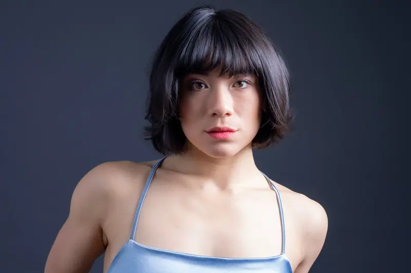 A modern and artistic portrait of a young adult woman with short hair in a light blue top against a dark backdrop.