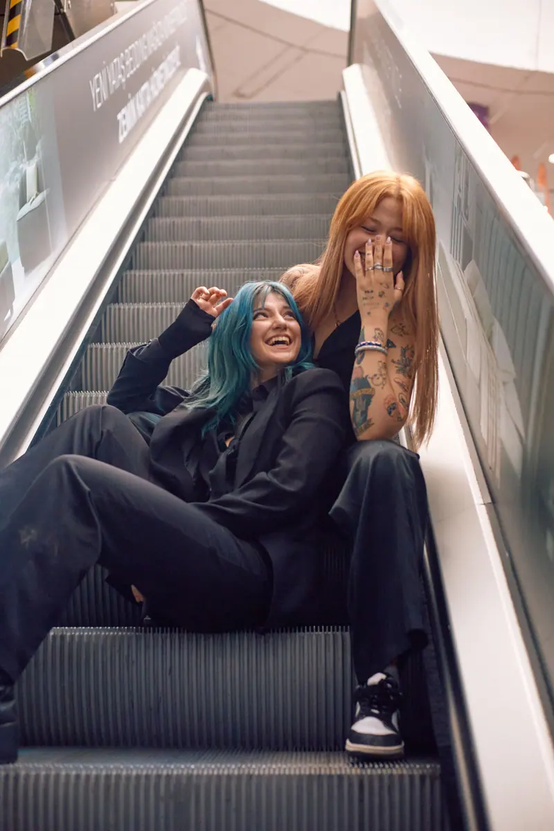 Two fashionable friends with colorful hair share a joyful moment on an escalator in Istanbul, Turkey.