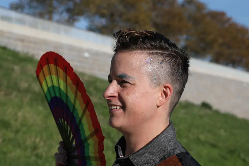 Smiling man with a fresh taper holding a rainbow fan