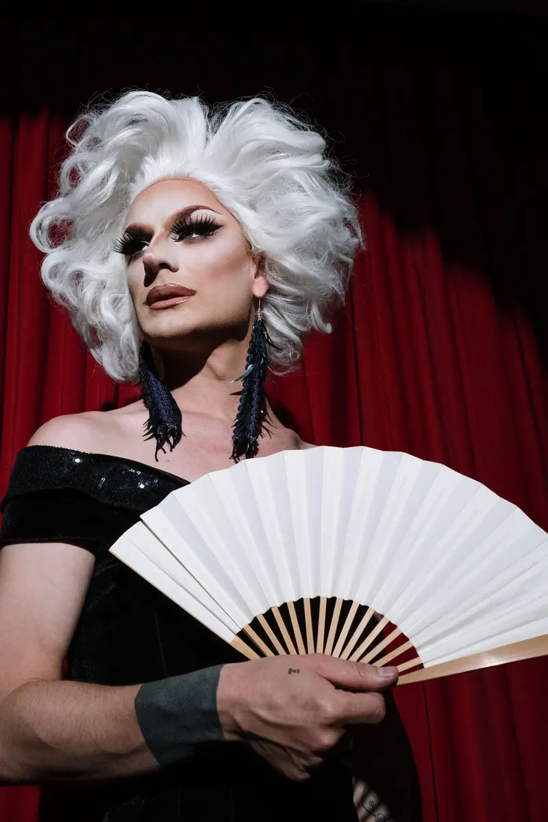 Platinum wig and a white fan against a red stage curtain