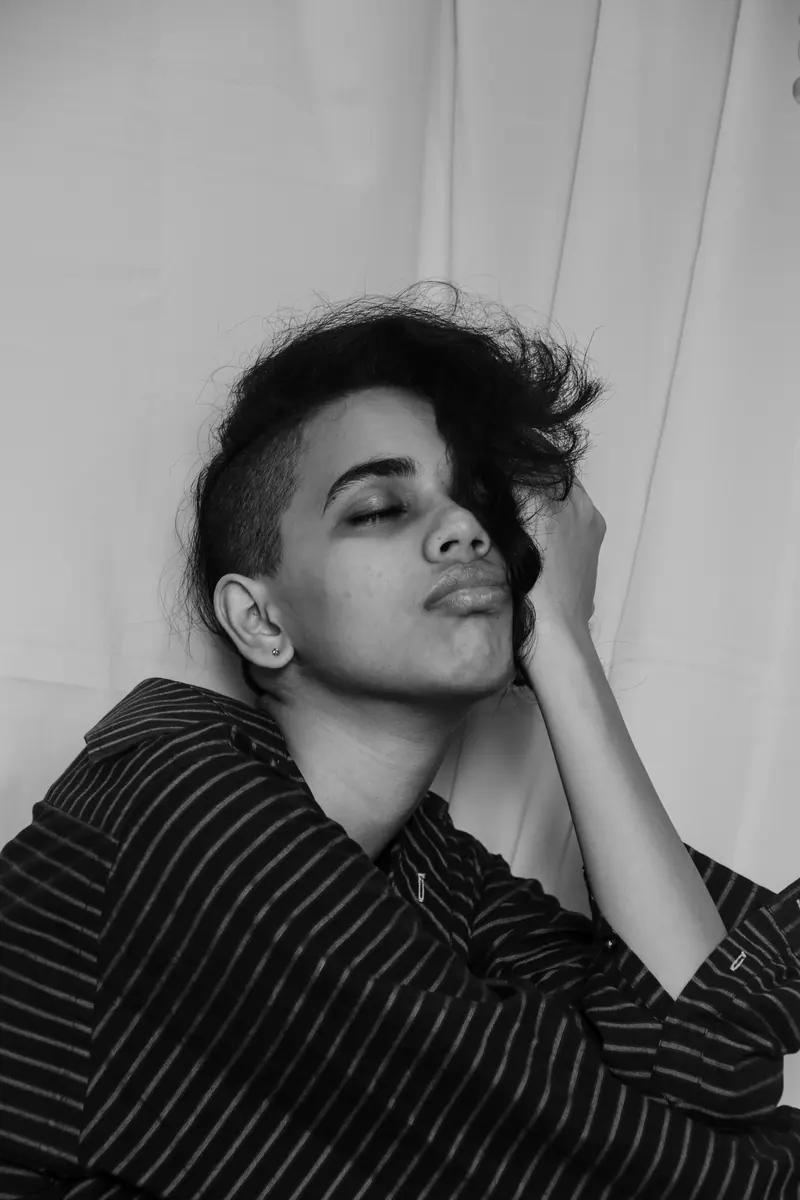 Monochrome portrait of a woman with eyes closed, wearing a striped shirt and undercut hairstyle.