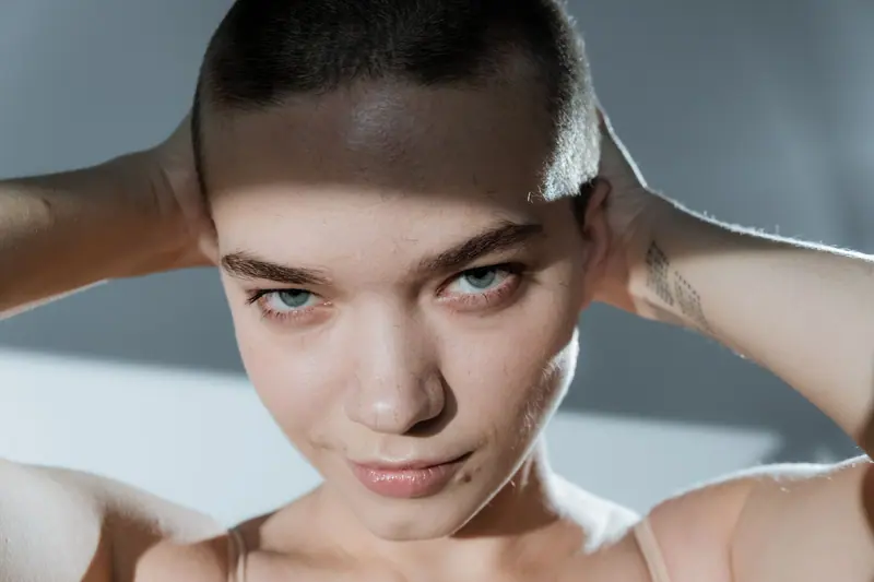 Close-up of a confident woman with a buzz cut, posing in studio light.