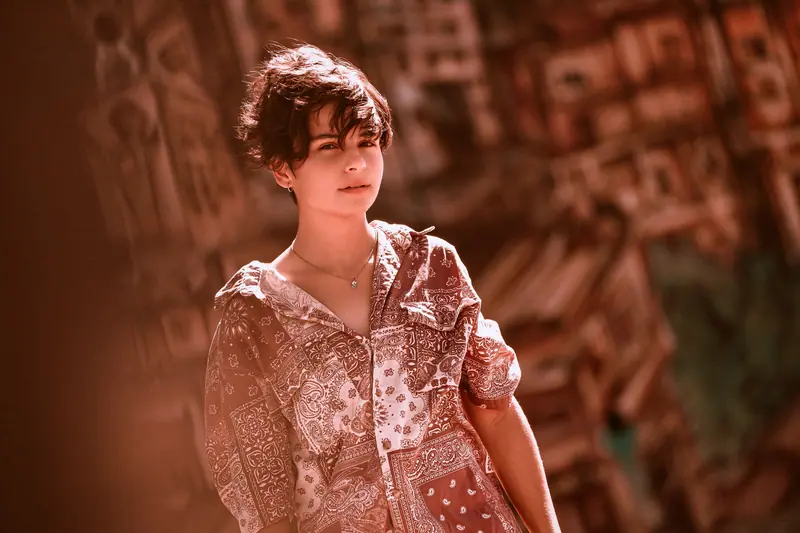 Young woman in patterned shirt, exuding a modern urban style against a cityscape backdrop.