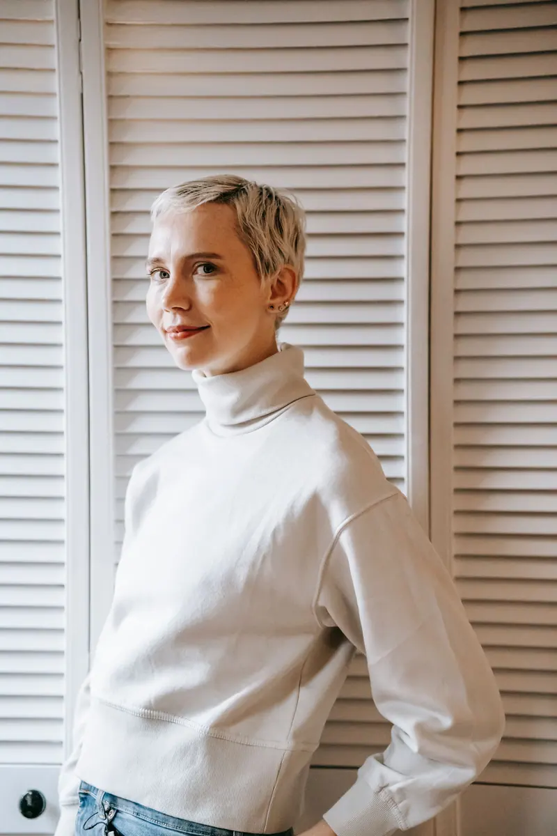 A stylish woman with a pixie cut and sweater poses elegantly indoors, exuding charm.