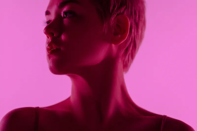 Close-up portrait of a woman with short hair in neon pink lighting, creating a modern, artistic atmosphere.