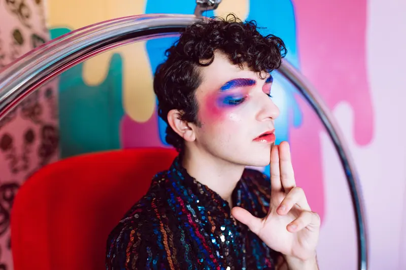 A vibrant portrait of a young person with bold makeup and a colorful background, exuding artistic expression.