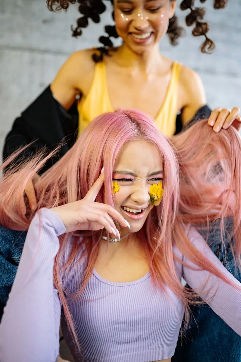 Two women enjoying a fun moment with vibrant hairstyles and floral accents indoors.